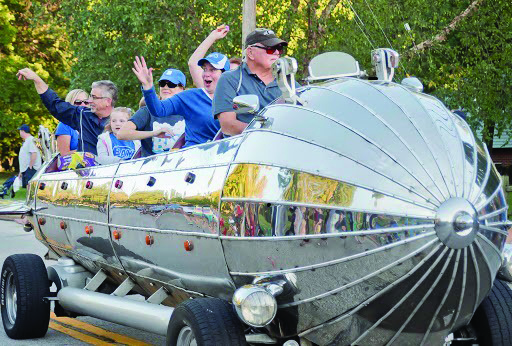 homecoming parade with a silver rocket mobile and folks inside it waving to the crowd