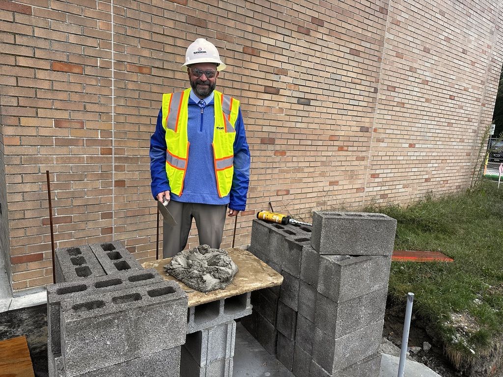 A man in a hard hat and yellow safety vest prepares a brick for placement at a construction site.