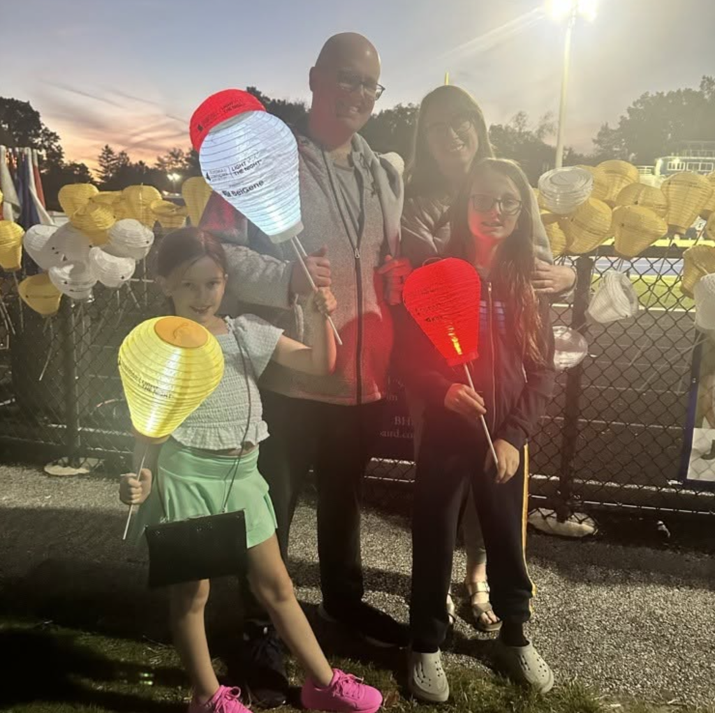 A family of four with four luminaria at dawn near a high school track.
