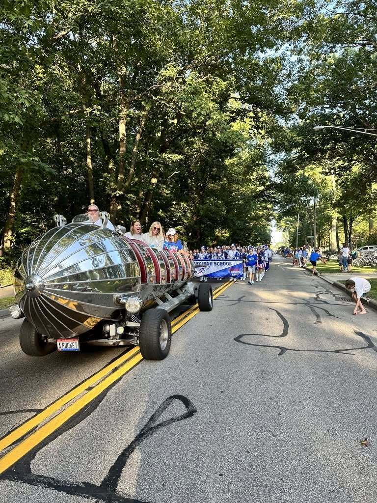 A homecoming photo with a silver rocket vehicle and the marching band.