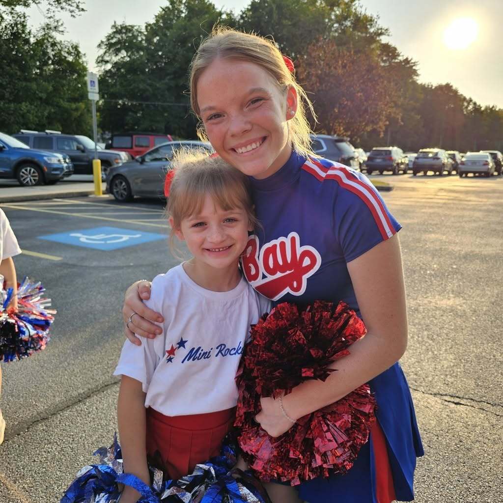 Homecoming photo of a cheerleader and a mini cheerleader with red, white and blue uniforms and poms.