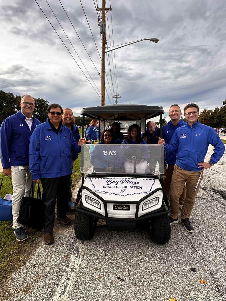 The Board of Education sitting in and standing near a golf cart lined up and ready for the homecoming parade.