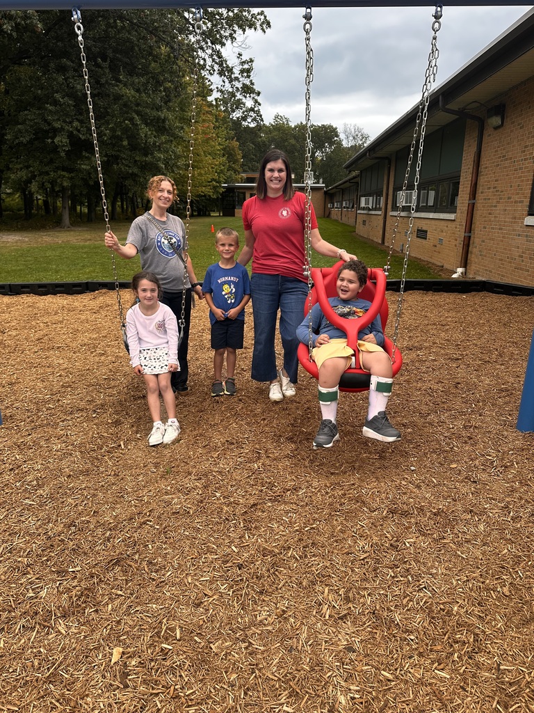 Two teachers and three students enjoy the new adaptive swing set on a playground. 