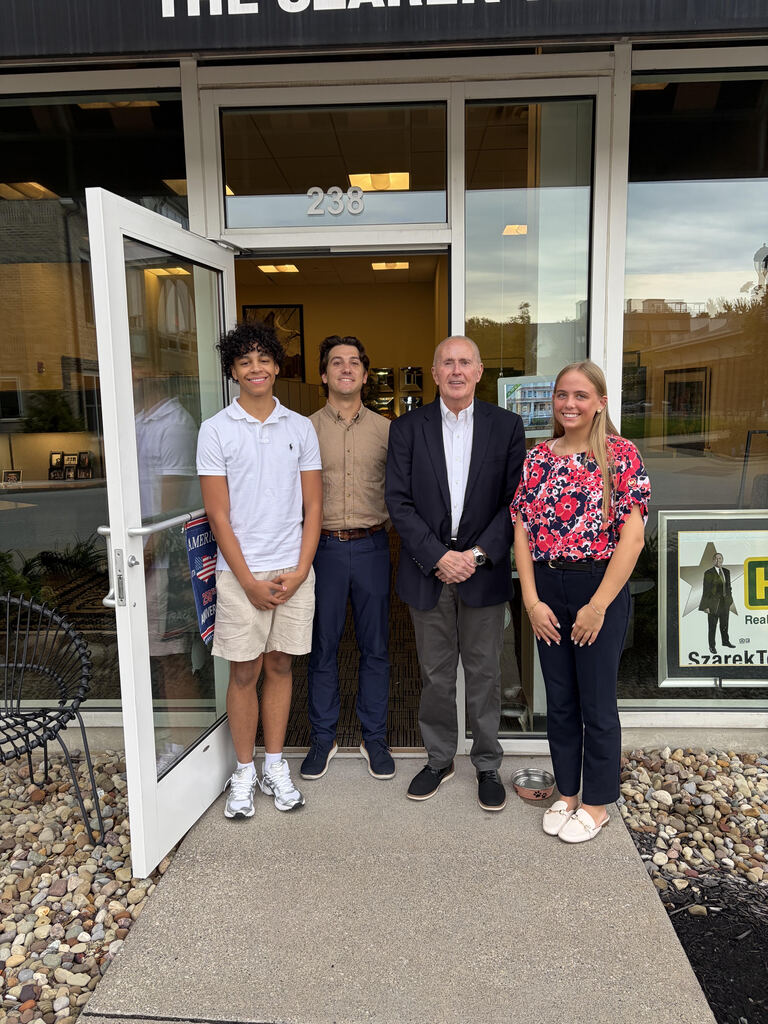 Two students and two adults pose for a photo in the doorway of the real estate office where the students shadowed.