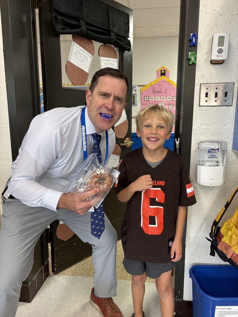 A principal and a student celebrate an October birthday with vampire fangs and a spooky-eyed donut.