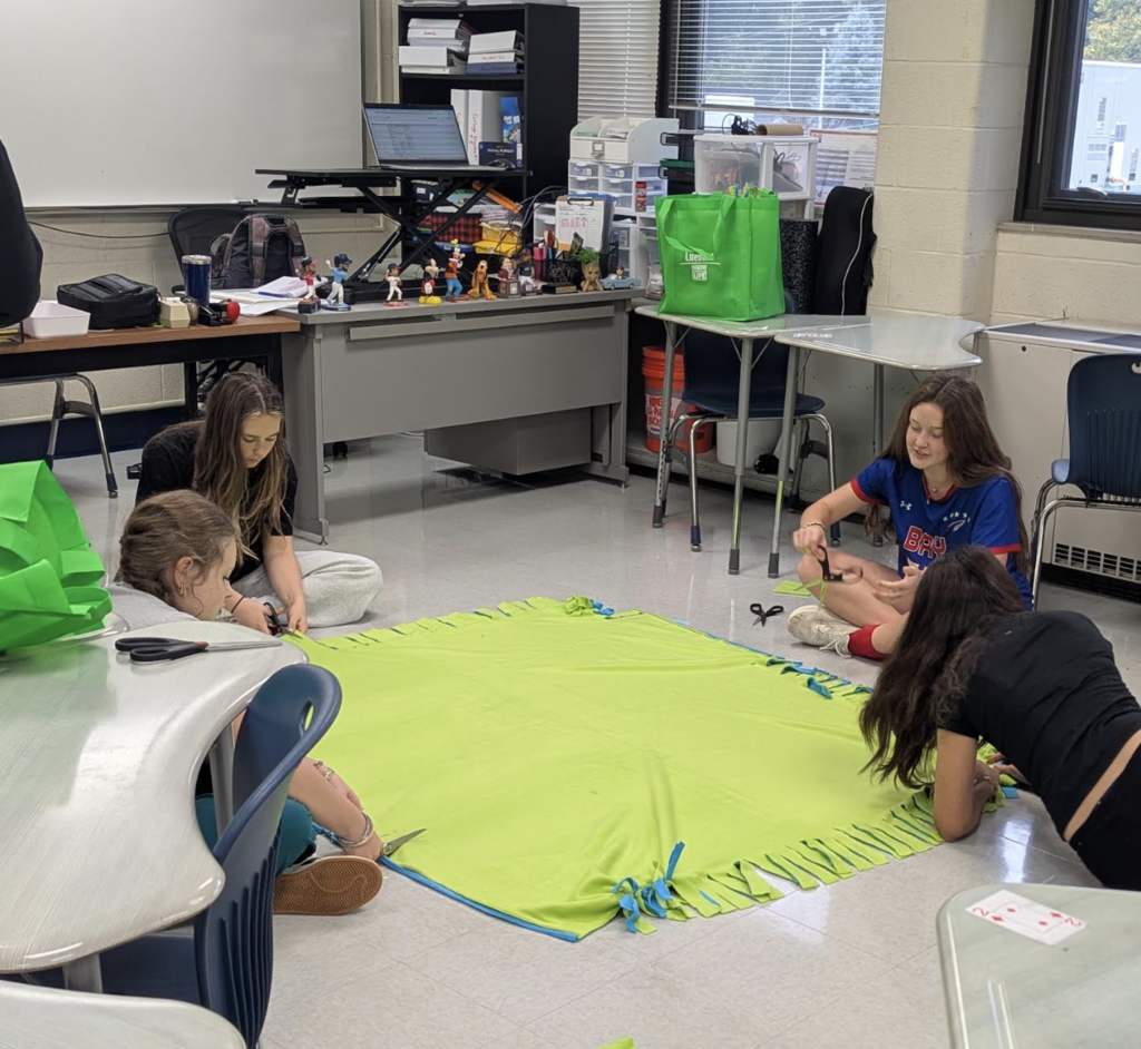 Four students seated on the floor making a tie blanket.
