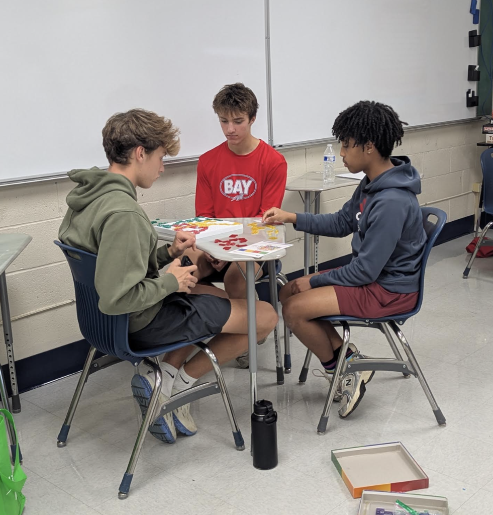 Three students seated around a table playing a game.