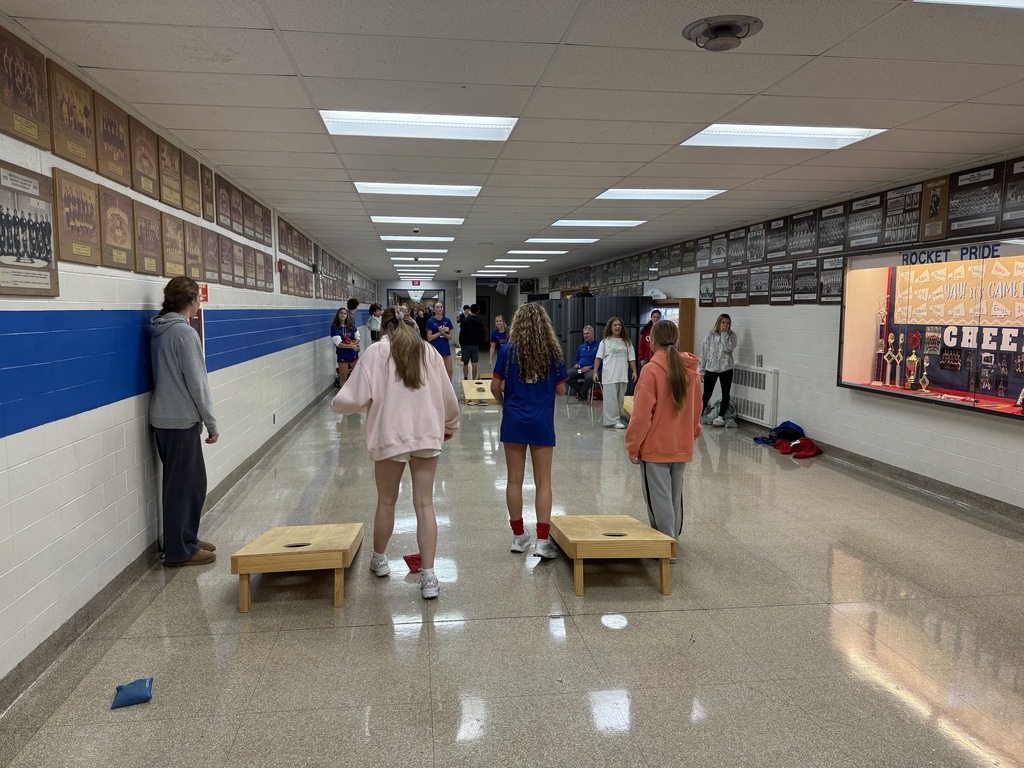 Students lined up playing corn hole in the hallway of their school.