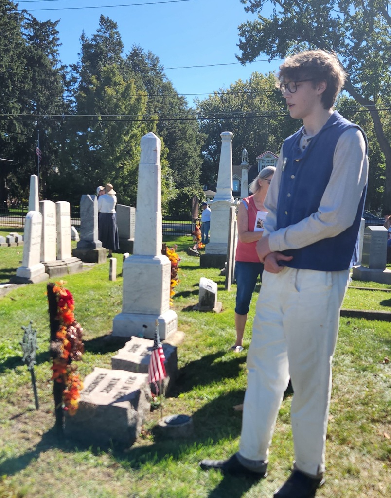 A student standing in an old cemetery dressed in colonial garb.