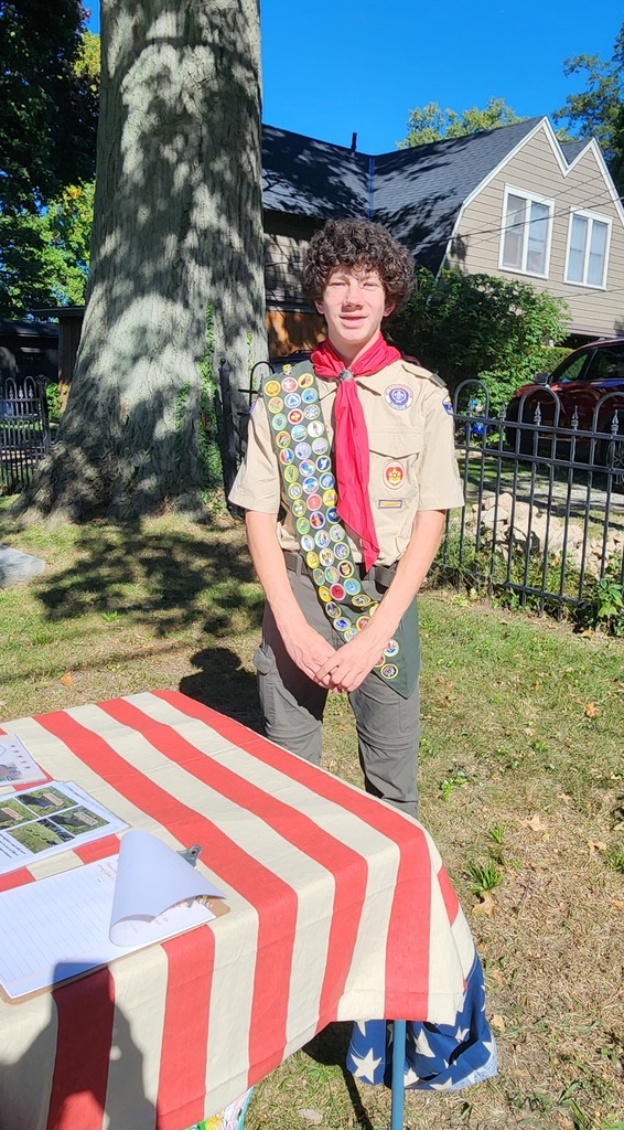A high school student in his boy scout uniform standing bay a table in a cemetery.