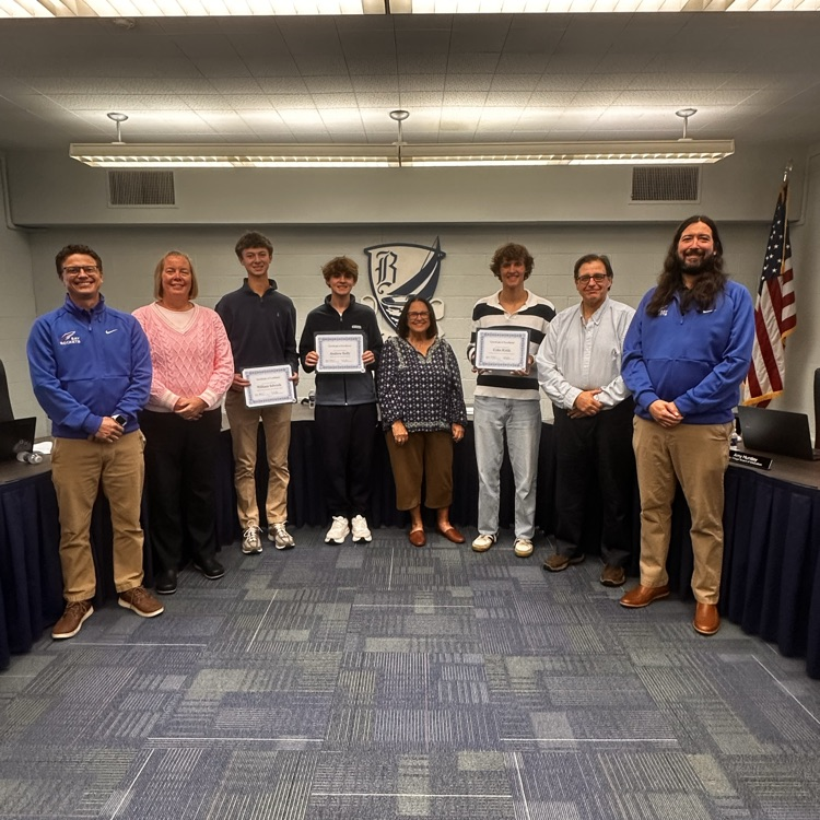 five board members surrounding three high school students as they are recognized at a board meeting