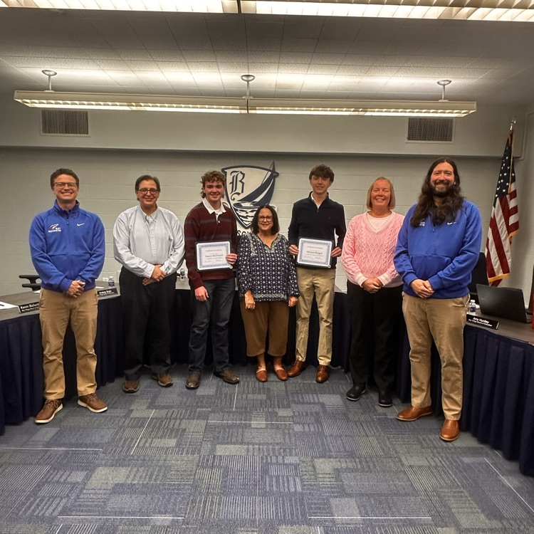 five board of education members standing by two high school students as they receive certificates for being recognized for their achievements