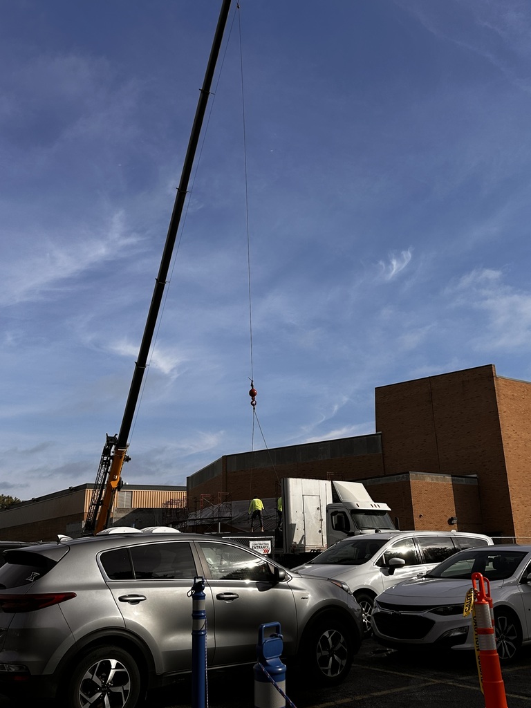 A crane carries a steel beam over to a high school construction site.