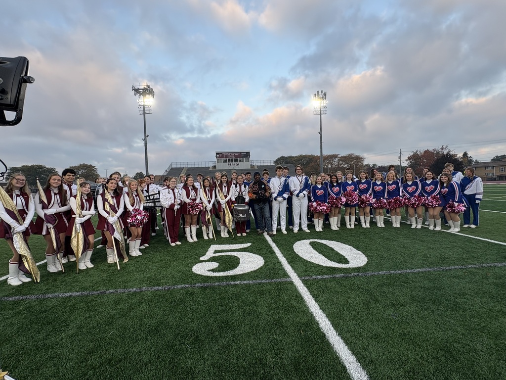 Two high school marching bands lined up on the 50-yard line on a football field.
