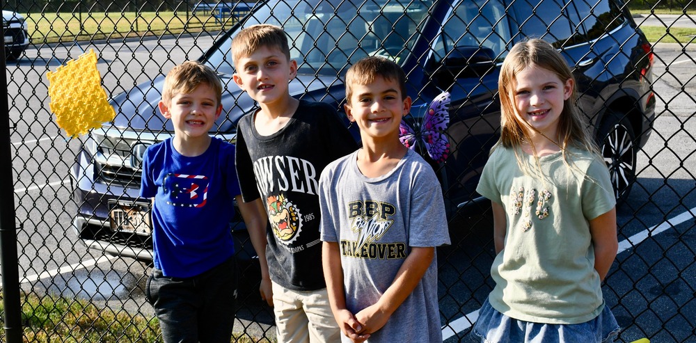 A group stands by a black vehicle in a parking lot, and posing together.