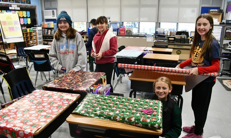 smiling students decorate classroom desks with festive holiday wrapping paper.