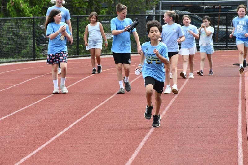 Students dressed in blue running on track.