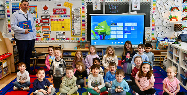 Students sitting on carpet with teacher smiling.
