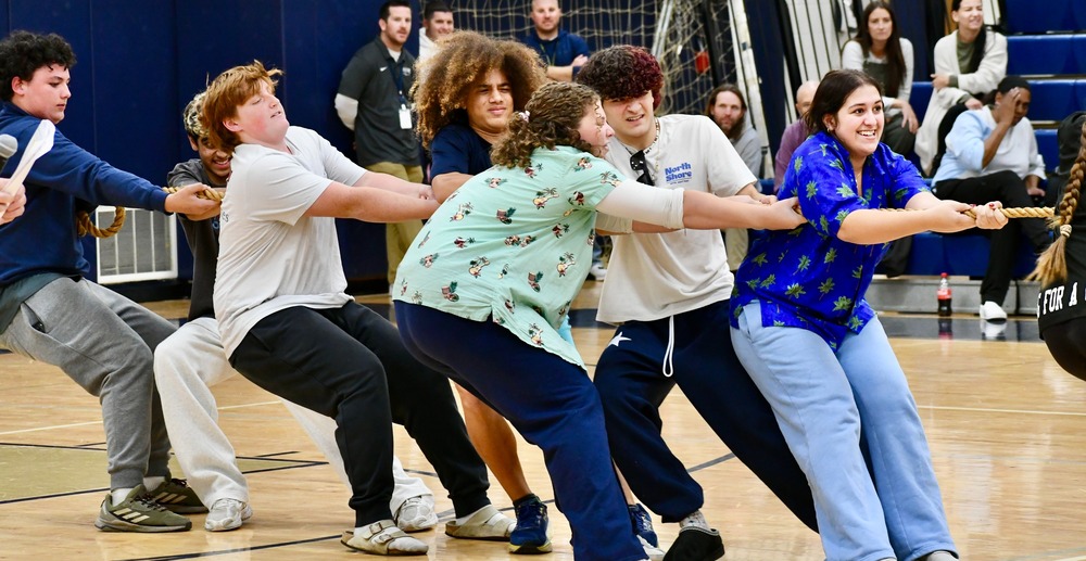 A group of people participates in a tug-of-war competition in a gymnasium setting.
