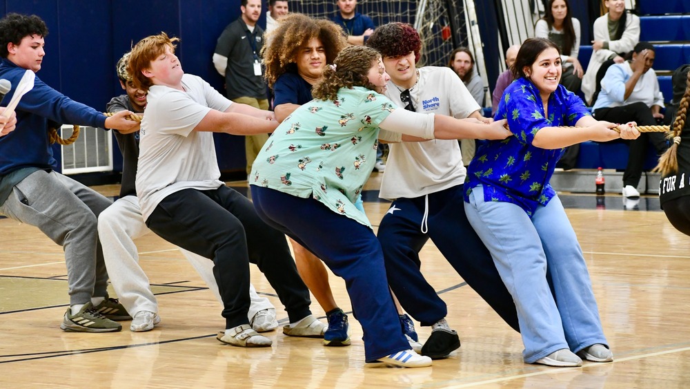 A group of people participates in a tug-of-war competition in a gymnasium setting.