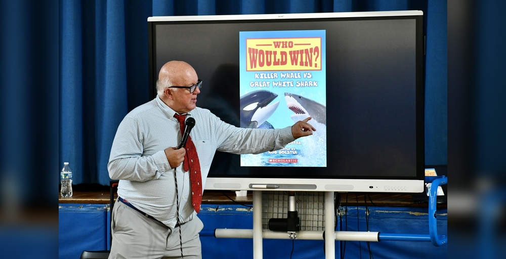 A person presents information about a book featuring a killer whale and a great white shark.