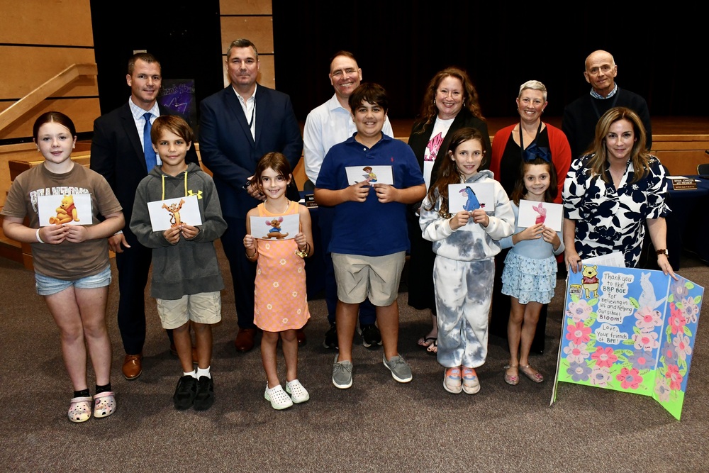 Students holding their art while standing in front of board members.