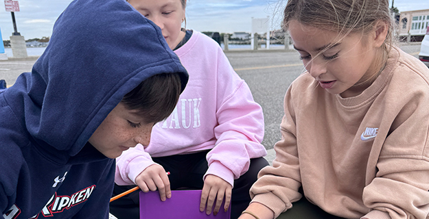 Students outside looking through box.