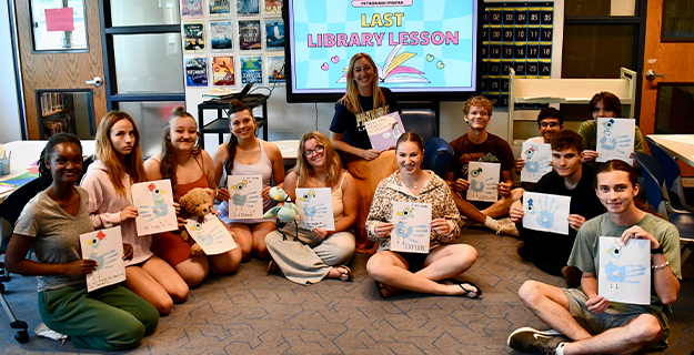 Students holding their projects, sitting on the ground.