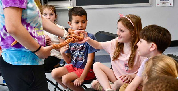 Student petting snake that is being held by instructor.