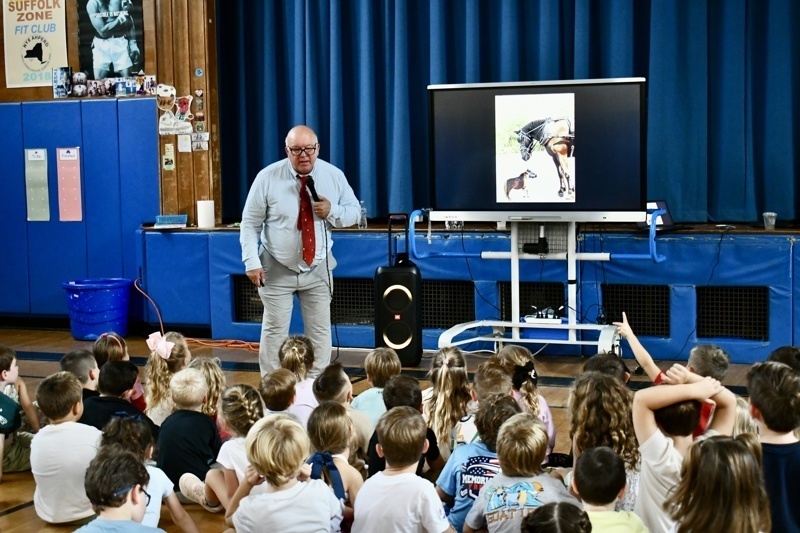 A person stands in front of a screen displaying an image, addressing a group of people.