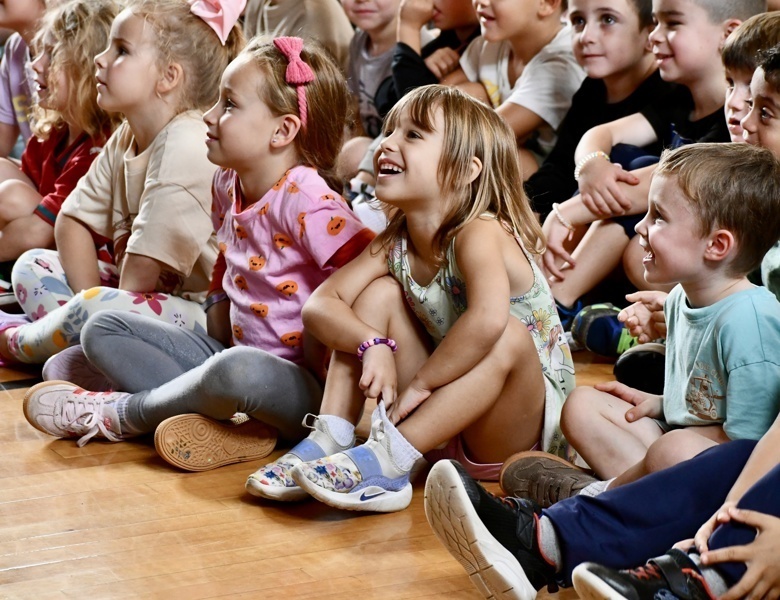 A group of children sitting on the floor, attentively watching an event or performance.