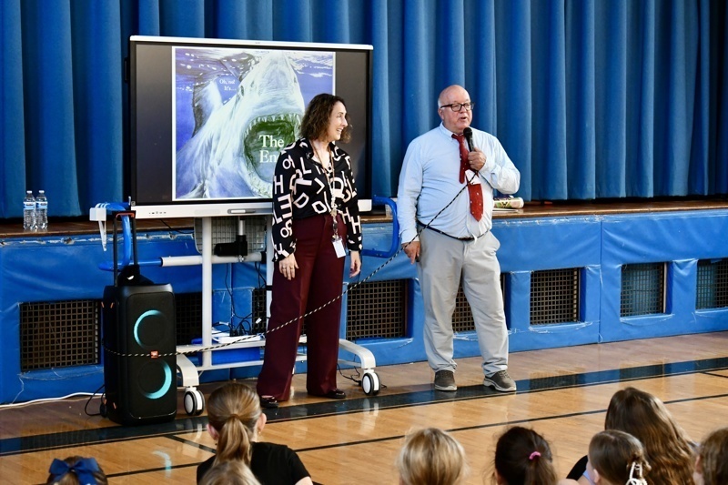 Two people present in front of a projector screen in a gymnasium setting.