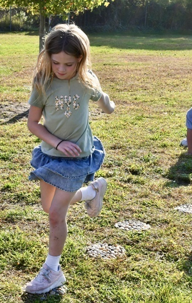 A child runs across a grassy field, wearing a green shirt and denim skirt.