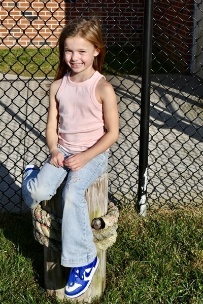 A person sits on a wooden post, leaning against a chain link fence outdoors.