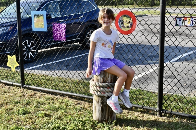 A person sits on a wooden post by a fence with colorful artwork and a vehicle.