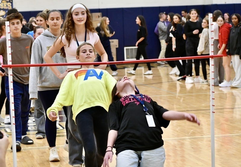 A group of people participates in a limbo contest in a gymnasium setting.