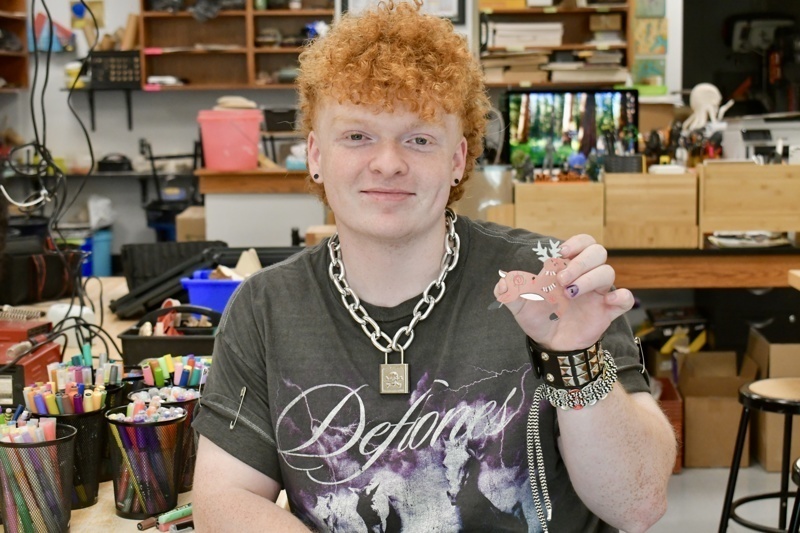 A person shows their handmade art piece in a creative workspace filled with supplies.