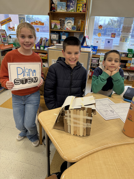 Children engaged in a classroom activity, working collaboratively with craft materials like popsicle sticks and masking tape. The atmosphere is focused and creative.