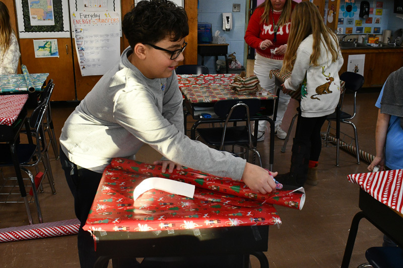 smiling students decorate classroom desks with festive holiday wrapping paper.