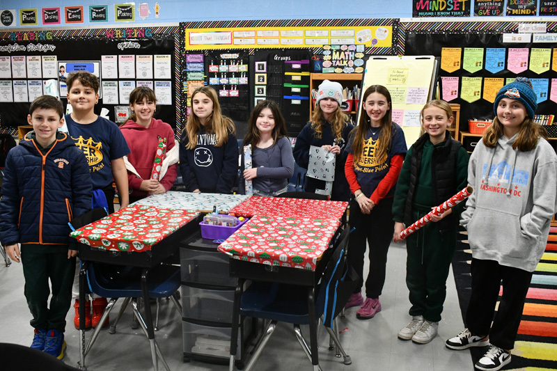 smiling students decorate classroom desks with festive holiday wrapping paper.