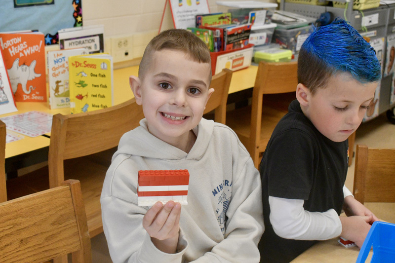  young children smiling at a classroom table, engaged in a playful activity.