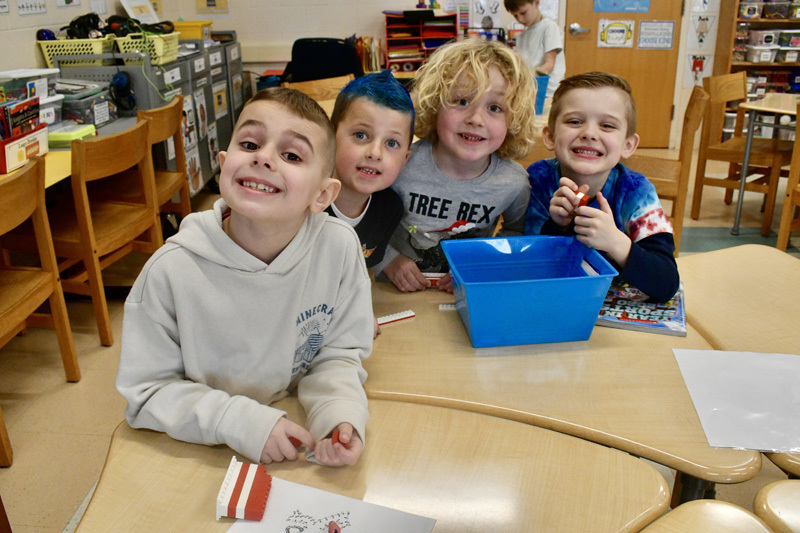  young children smiling at a classroom table, engaged in a playful activity.
