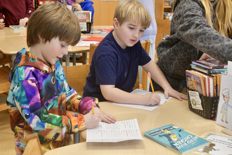  young children smiling at a classroom table, engaged in a playful activity.