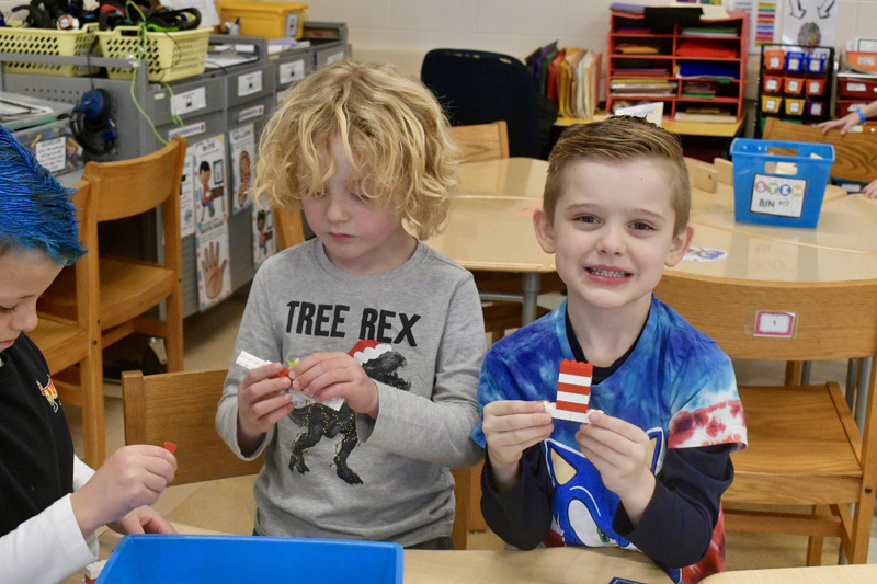 young children smiling at a classroom table, engaged in a playful activity.