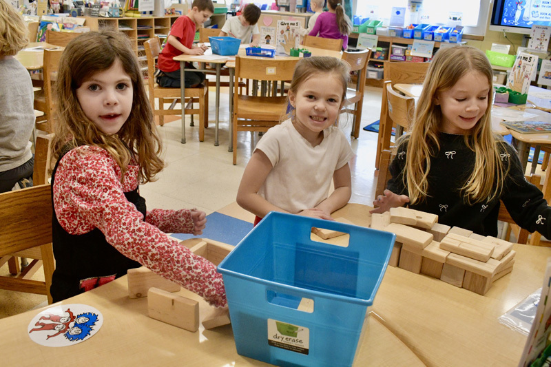 young children smiling at a classroom table, engaged in a playful activity.