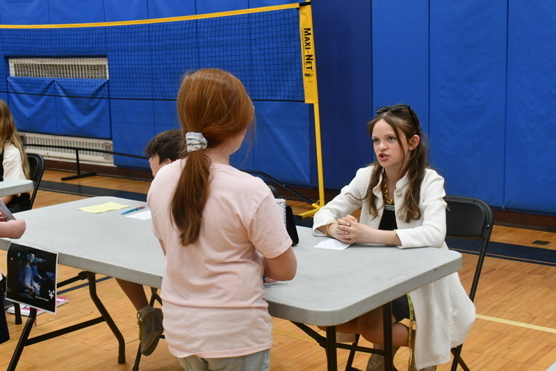 Young students engaged in a classroom activity, interacting at tables with props and costumes, fostering creativity and learning in a vibrant gymnasium setting.