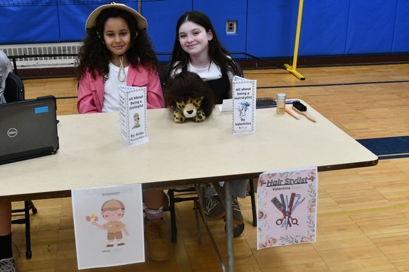 Young students engaged in a classroom activity, interacting at tables with props and costumes, fostering creativity and learning in a vibrant gymnasium setting.
