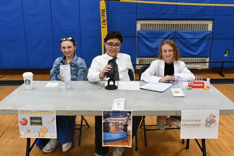 Young students engaged in a classroom activity, interacting at tables with props and costumes, fostering creativity and learning in a vibrant gymnasium setting.