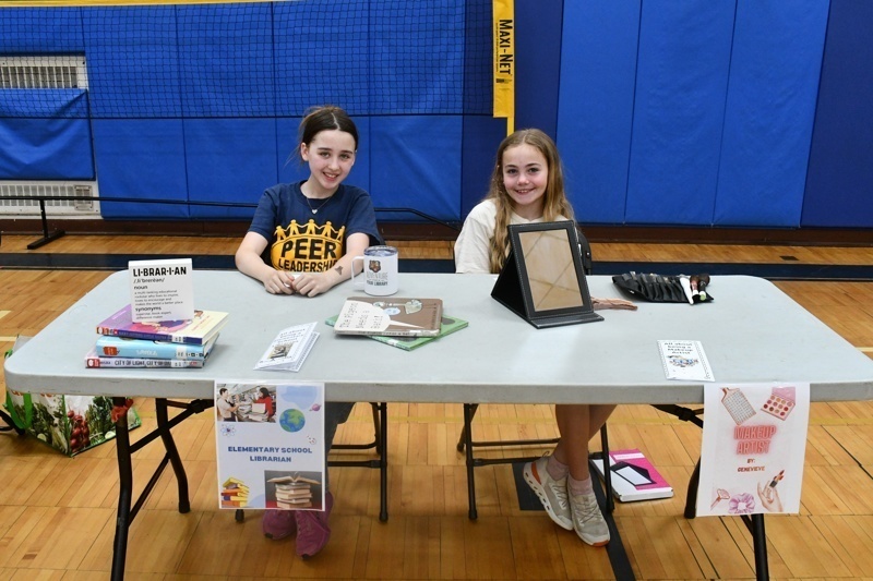 Young students engaged in a classroom activity, interacting at tables with props and costumes, fostering creativity and learning in a vibrant gymnasium setting.