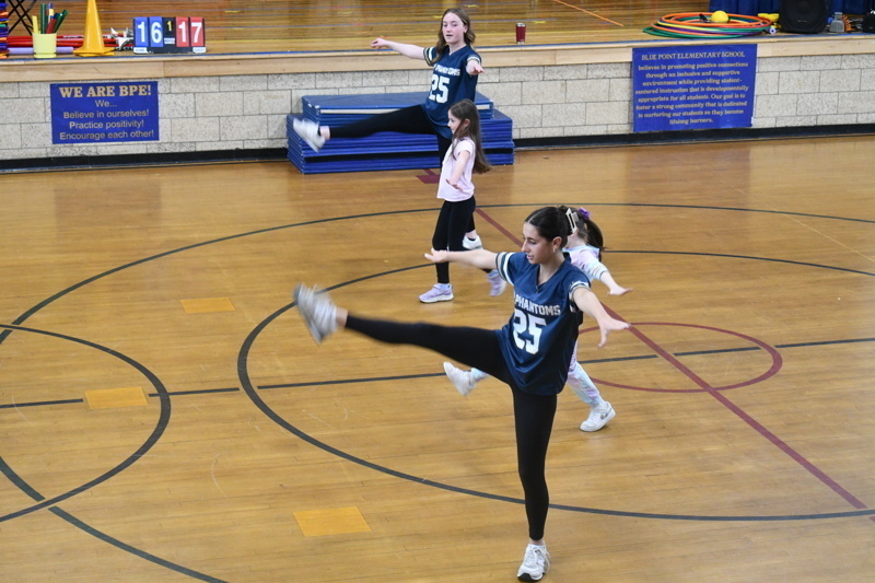 A group of young dancers in school uniforms perform a dance routine on a gymnasium floor, showcasing energetic movements and teamwork.